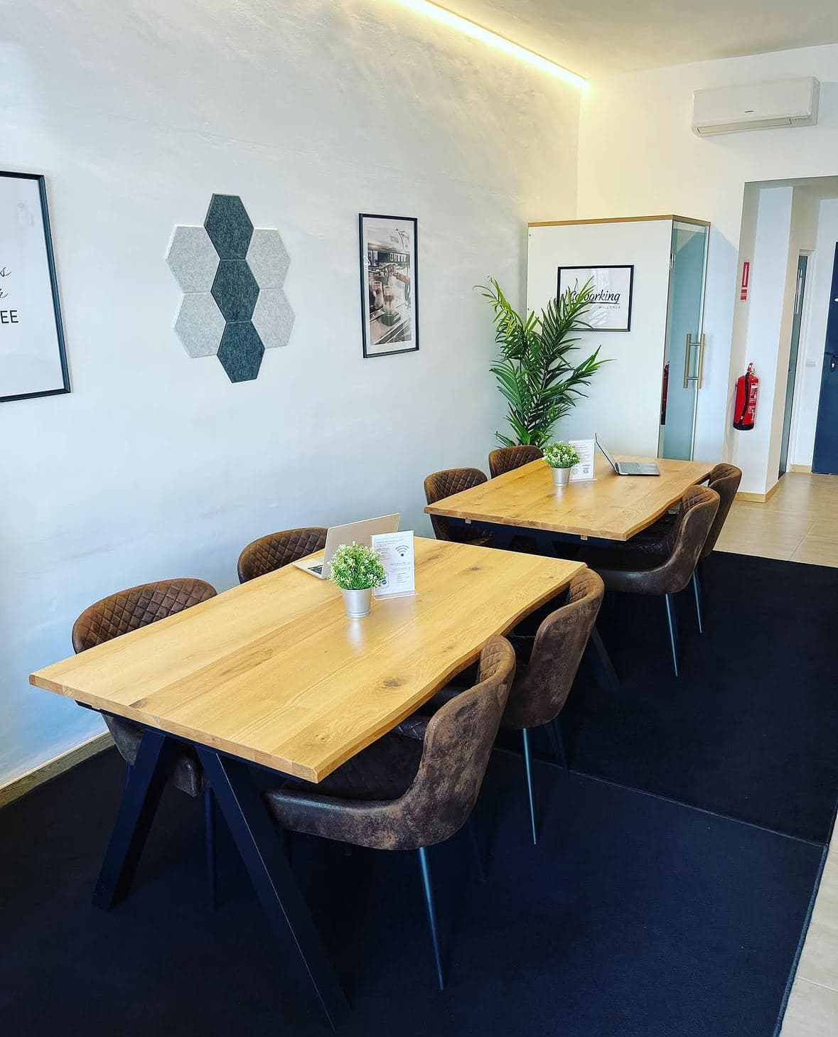 Zwei lange Eichentische mit Lederstühlen im Bereich für Tagesgäste, dahinter die Meetingbox